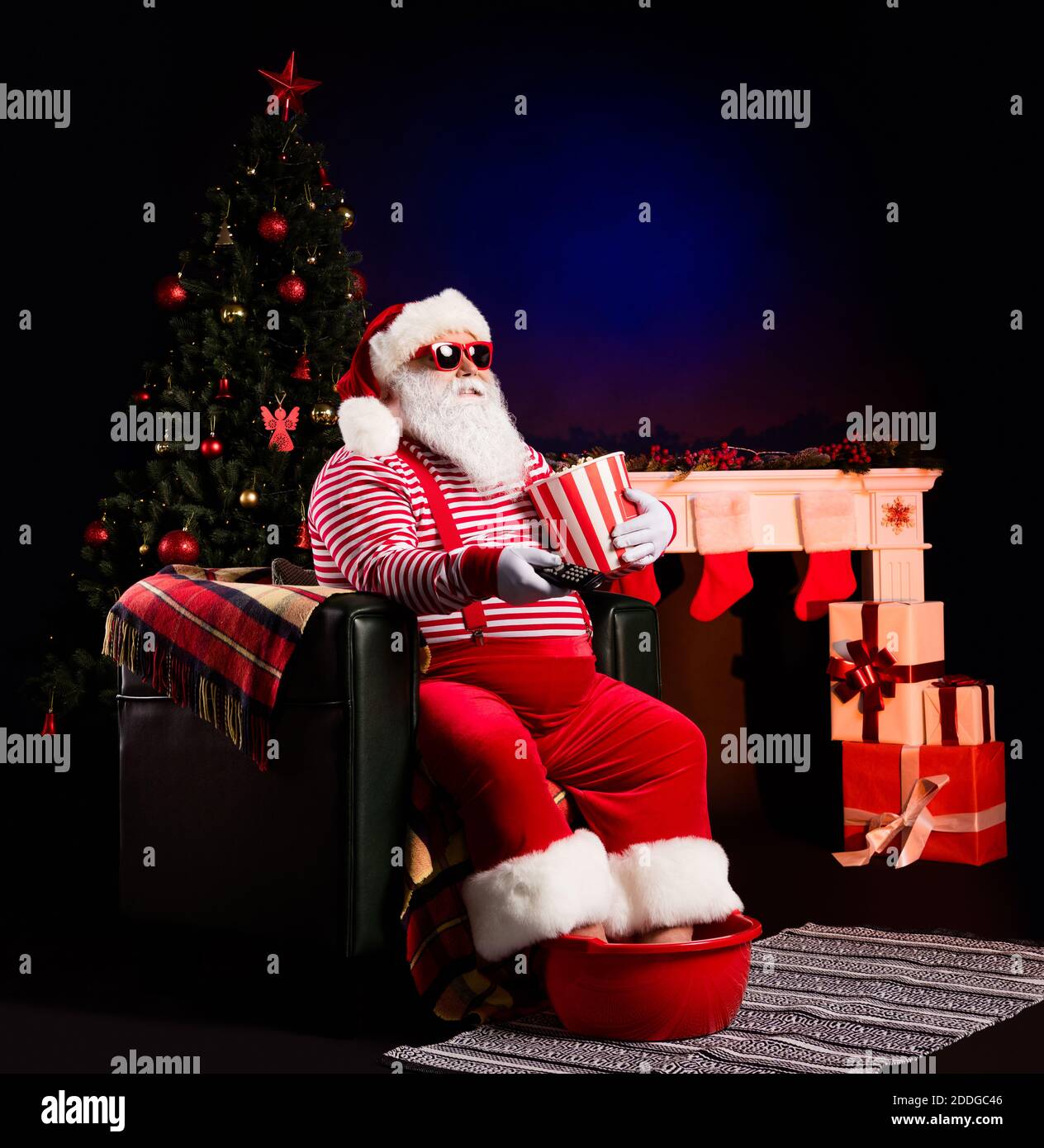 https://c8.alamy.com/comp/2DDGC46/funny-santa-hold-remote-control-popcorn-box-legs-basin-wear-x-mas-costume-cap-sunglass-isolated-decorated-black-background-2DDGC46.jpg
