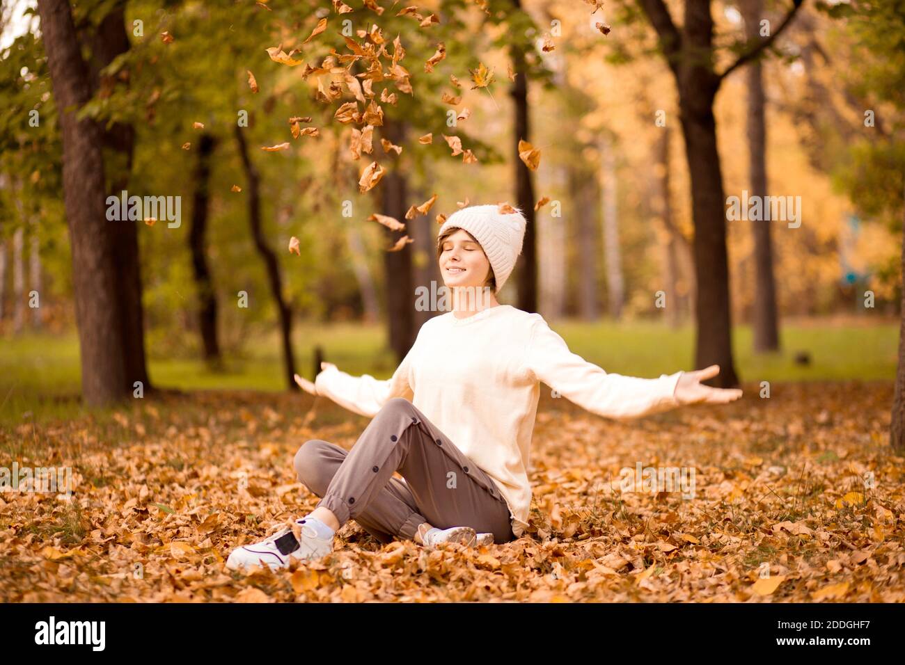Smiling happy teen girl portrait in white hat throws up leaves in autumn park. Stock Photo