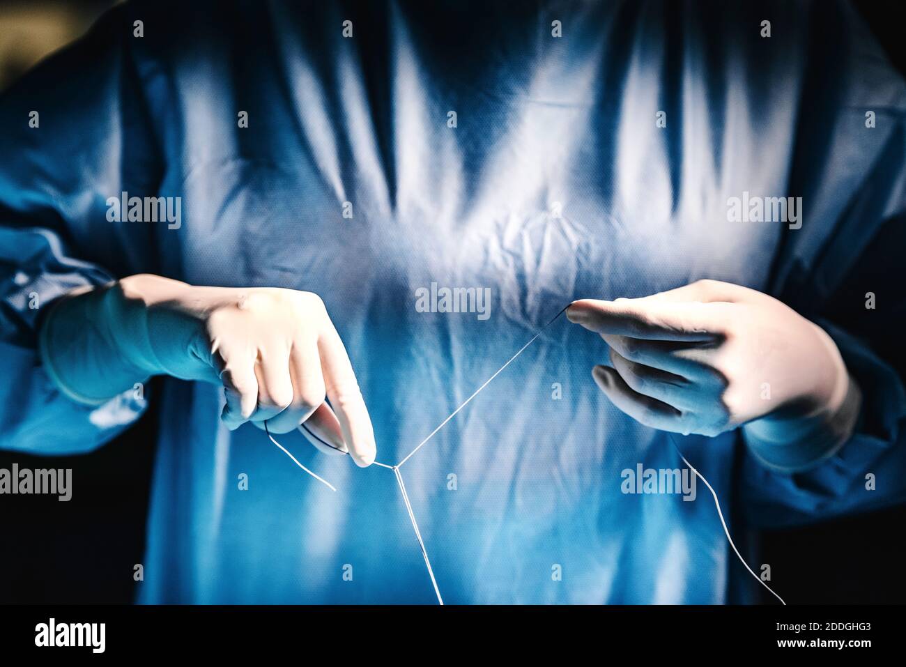 Picture of Crop anonymous medic in latex gloves tying knot with surgical thread ...