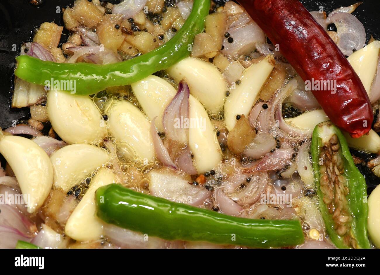 Sautéing or sautéing in a Mud Pan   Frying  garlic,turmeric,onions,green chilli and Mustard in oil in a Mud Bowl.South Indian kitchen food recipes. Stock Photo