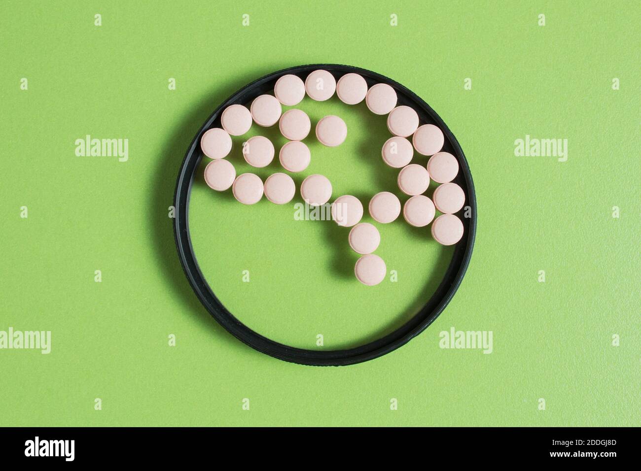 A brain made up of small round pills inside a circular lens on a green table. Health concept. Stock Photo