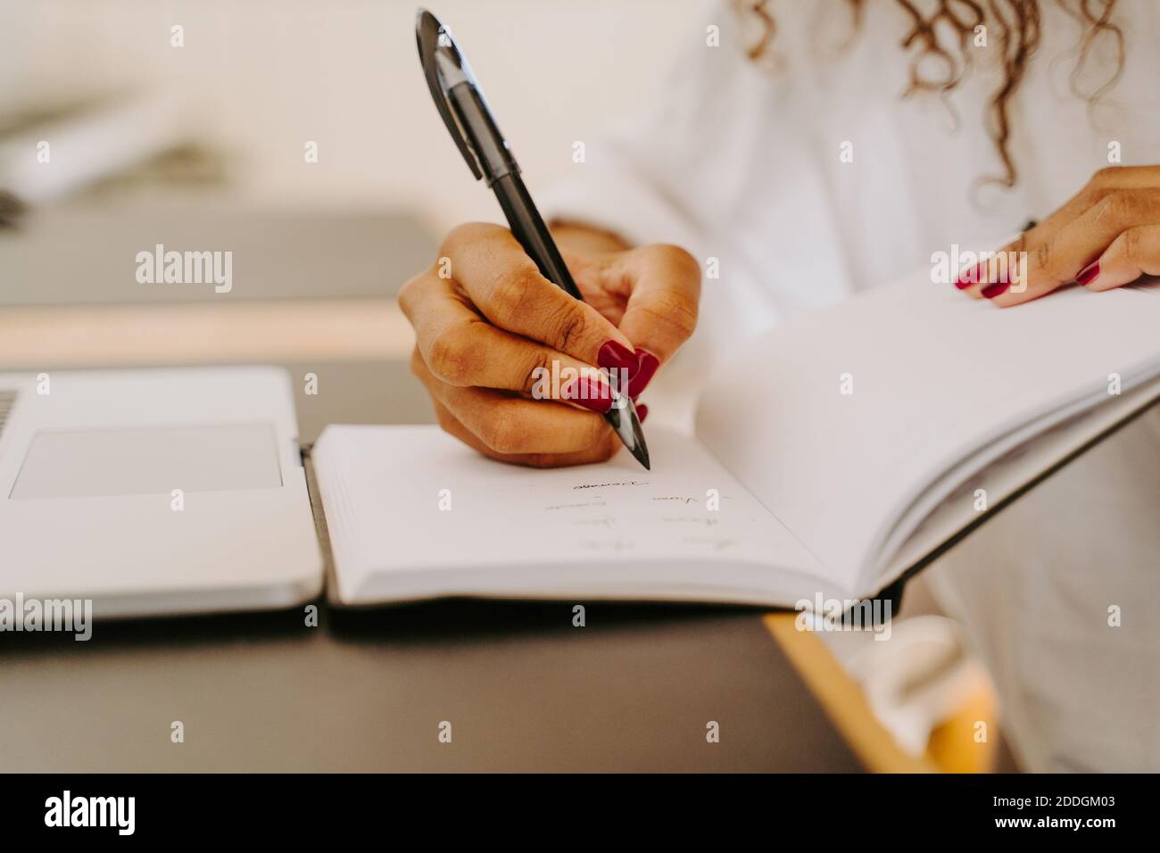 Crop unrecognizable female entrepreneur sitting at table with laptop and writing plan for business project in notebook Stock Photo