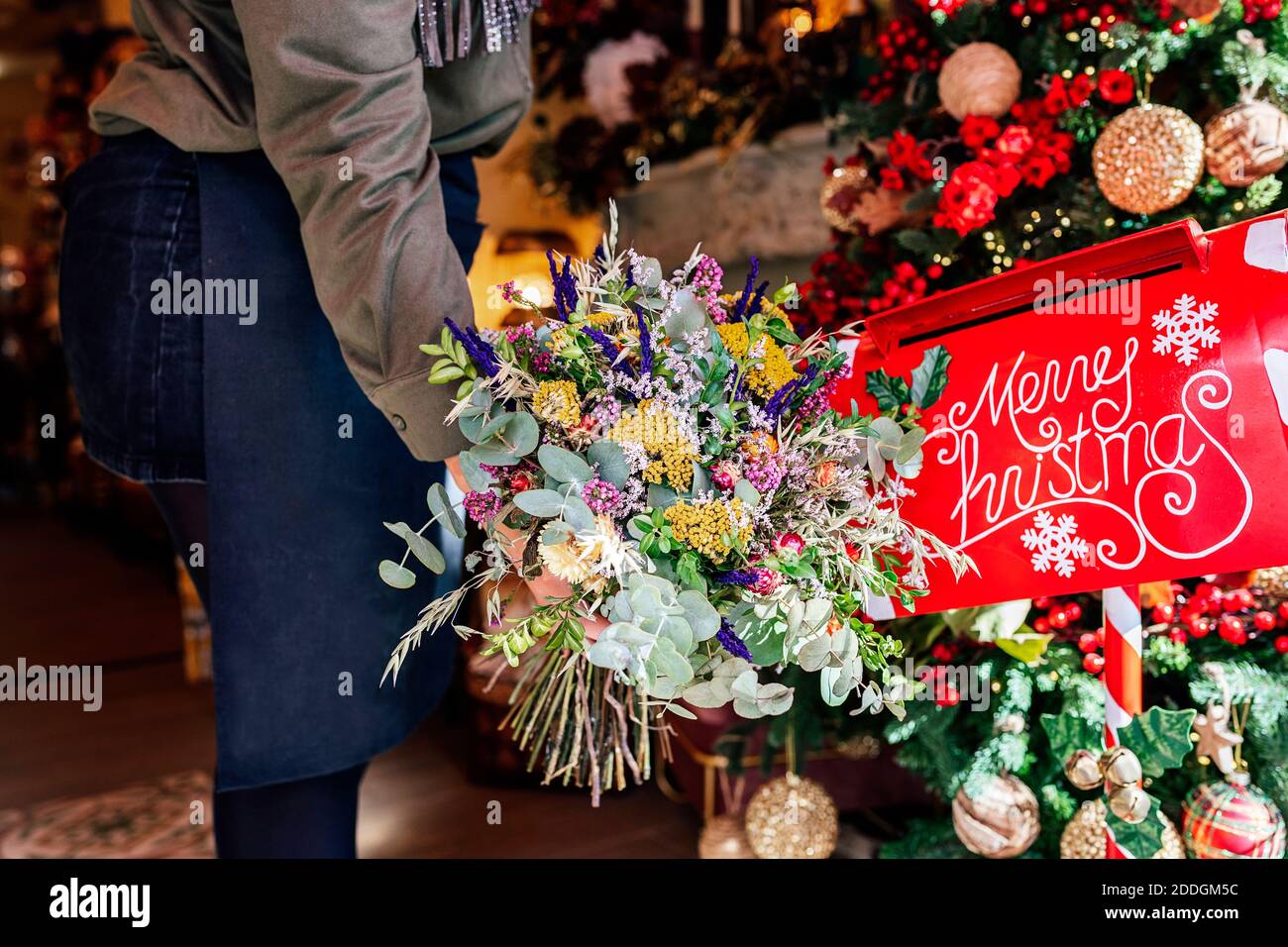 Cropped unrecognizable Woman holding flower bouquet standing in shop with christmas decorations near letter box Stock Photo