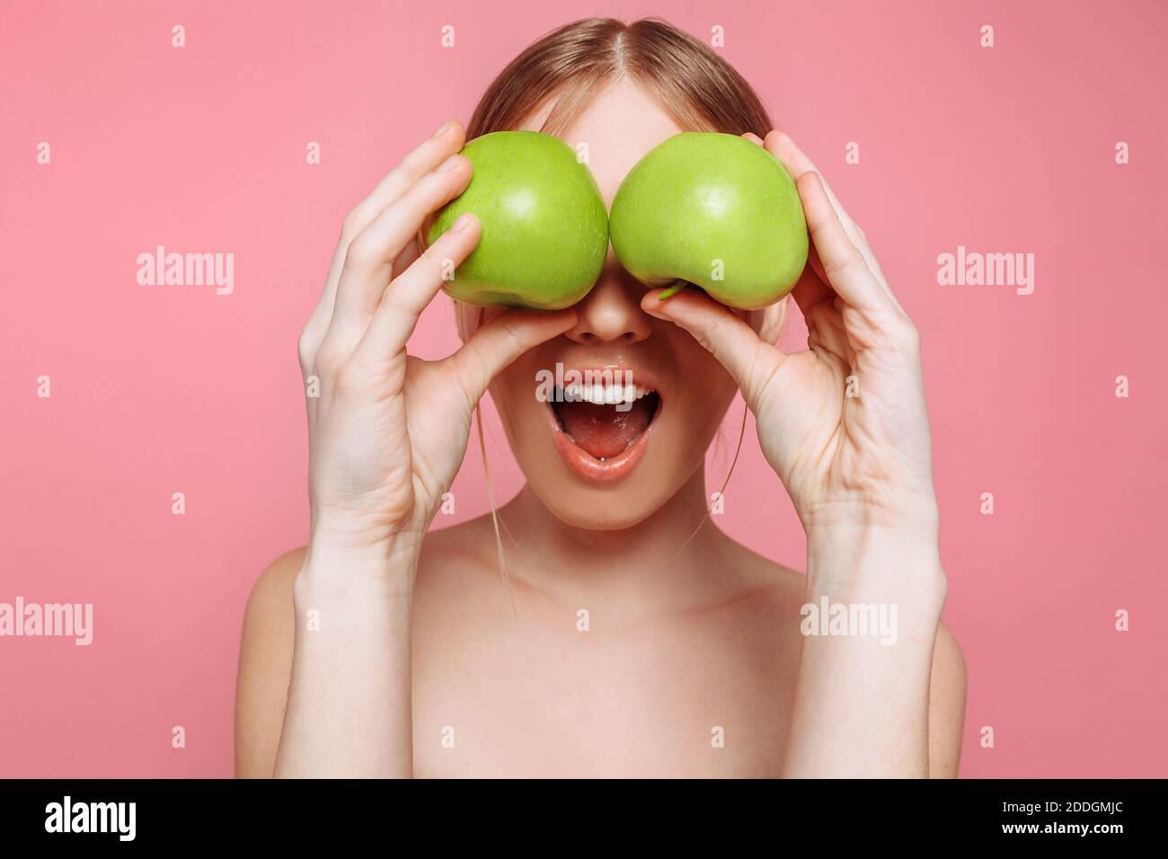 Portrait of a happy beautiful woman holding an apple, covering her eyes with apples, on pink background. Natural beauty concept Stock Photo