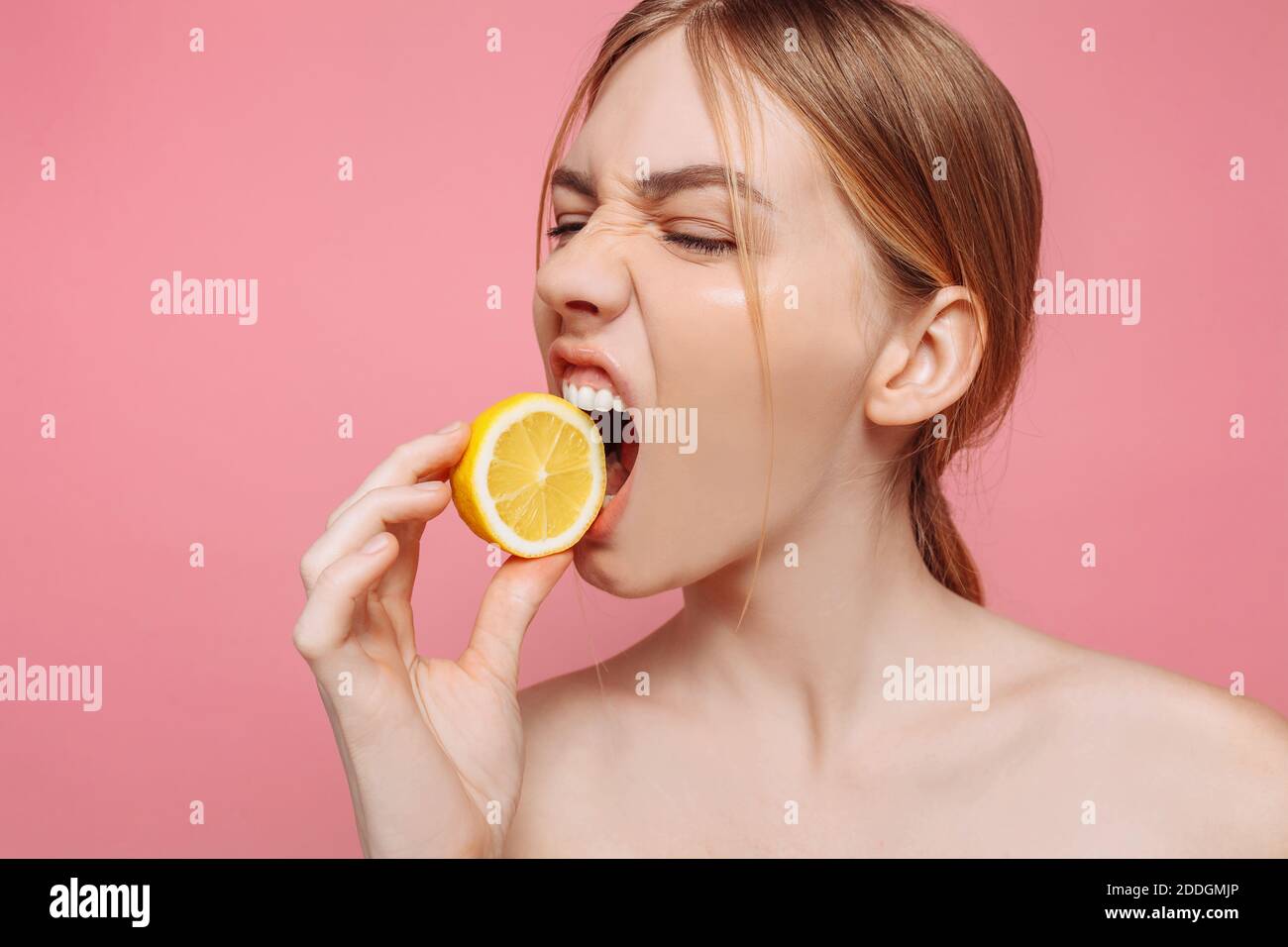 Portrait of a cheerful feminine girl, natural clear skin, girl with a piece of lemon, trying to bite him, isolated against a pink background. Skin car Stock Photo