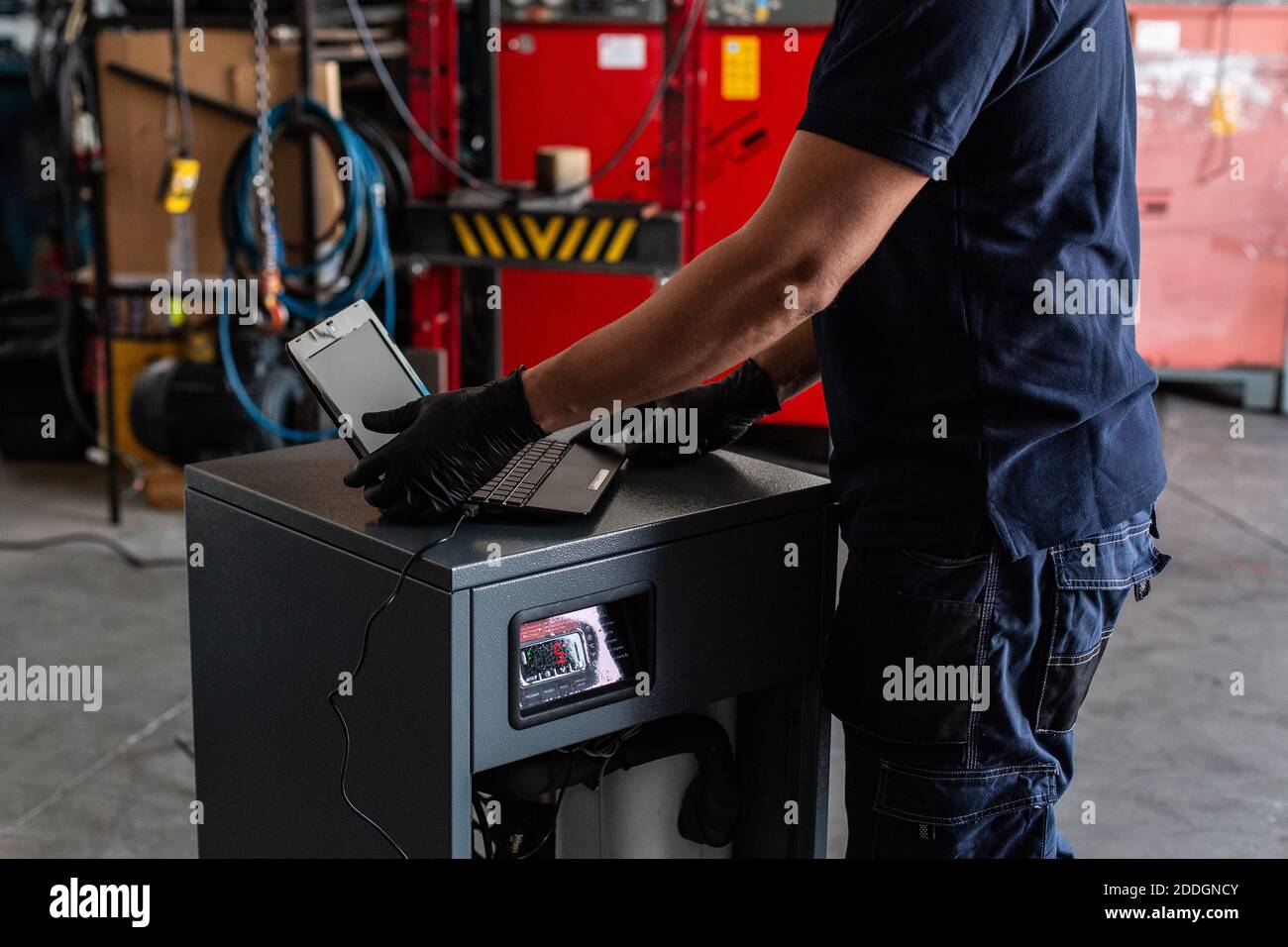 Unrecognizable adult man in using laptop to program broken machine during work in modern workshop Stock Photo
