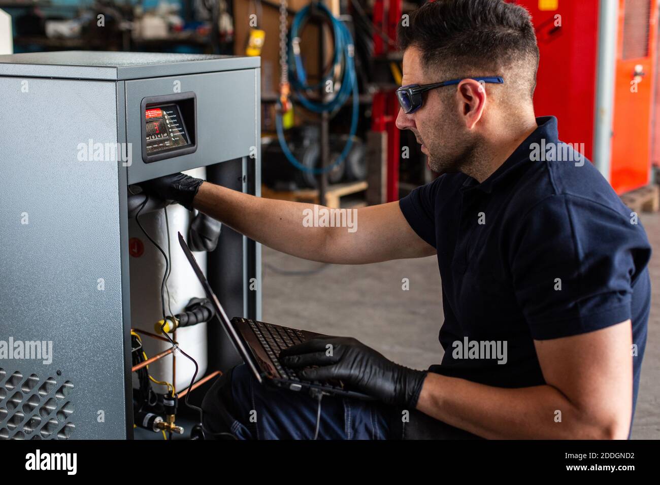 Adult man in goggles using laptop to program broken machine during work in modern workshop Stock Photo