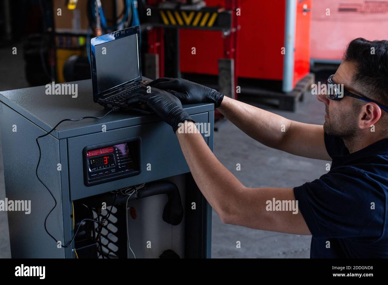 Adult man in goggles using laptop to program broken machine during work in modern workshop Stock Photo