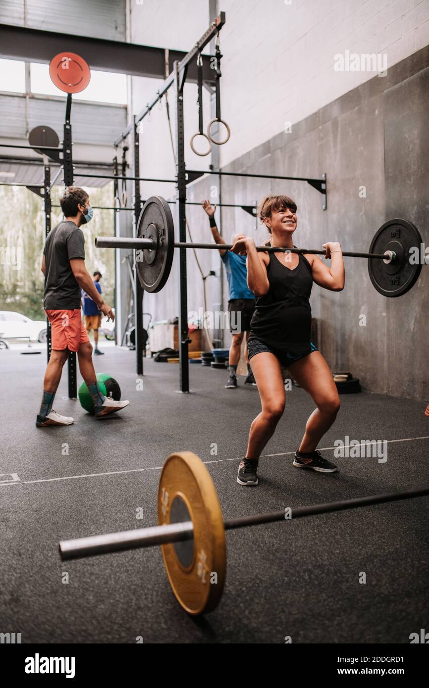 Athletic pregnant Woman doing exercises with barbell in gym during workout Stock Photo
