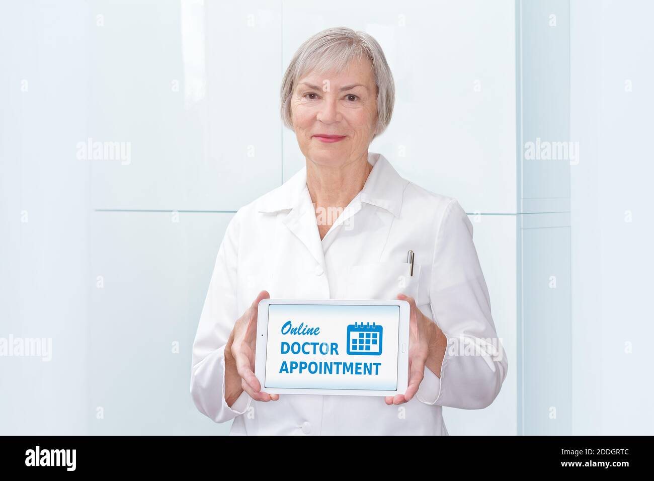 Friendly senior doctor showing a tablet computer with the text: online doctor appointment, light background. Stock Photo