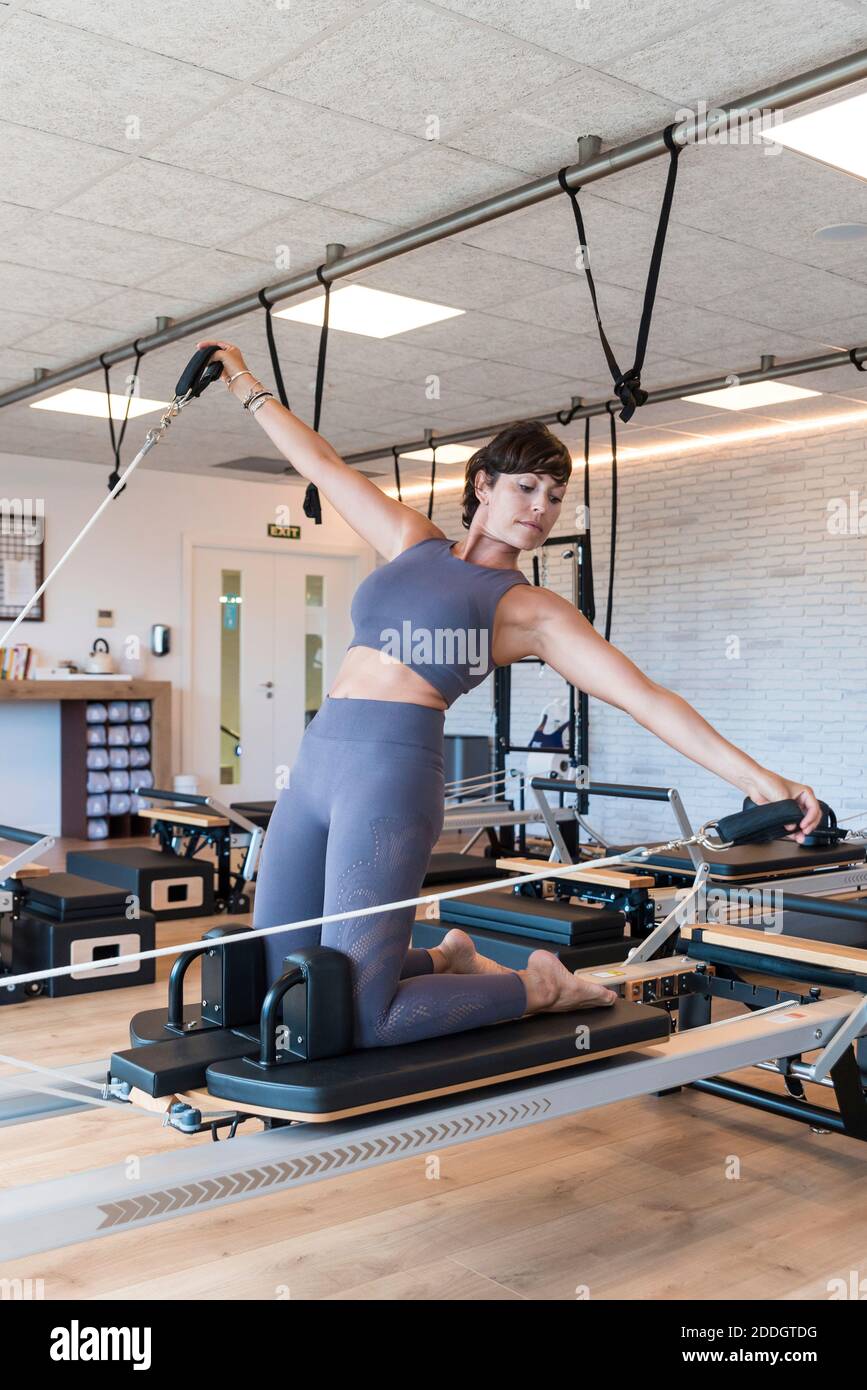 Fit adult female doing Kneeling Lean Back exercise with outstretched arms  on reformer during Pilates workout in gym Stock Photo - Alamy