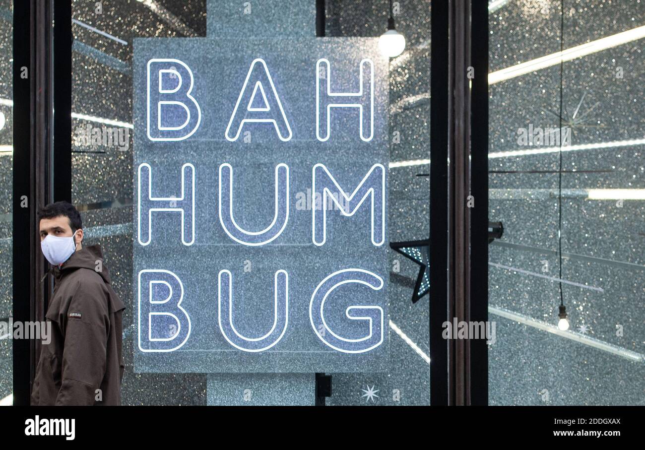 A man wearing a face mask passes a Christmas window display reading 'Bah Humbug', in central London, as England approaches the final week of a four week national lockdown to curb the spread of coronavirus. Stock Photo