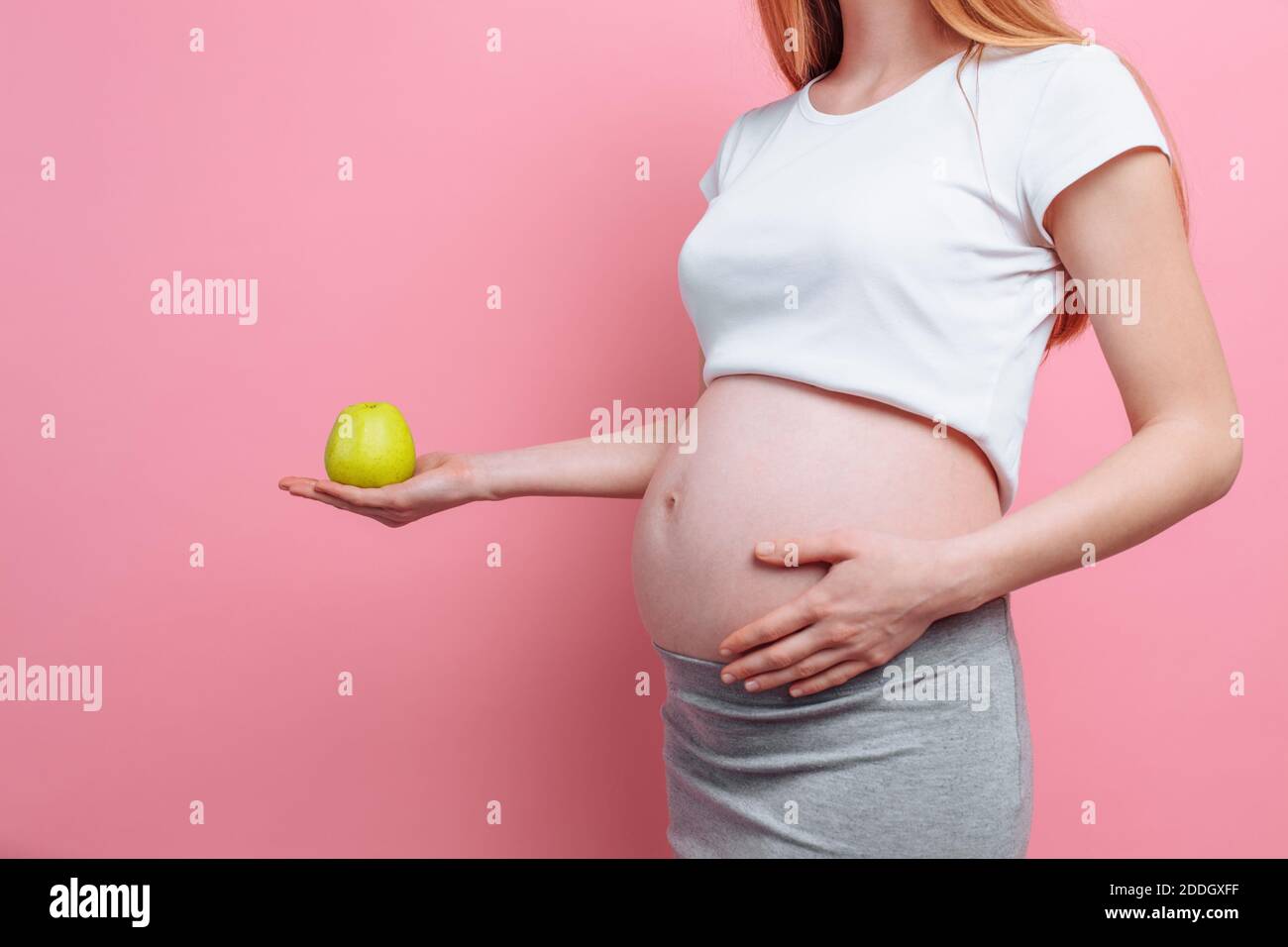 Pregnant woman holding a green apple near the belly. The concept of