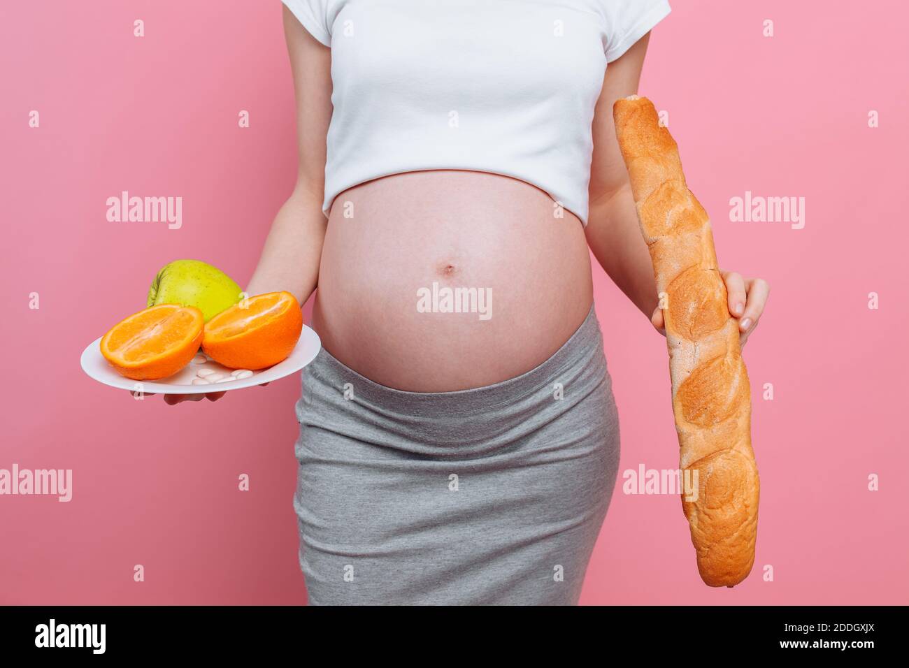Pregnant woman with a plate of fruit and a loaf of bread on a pink