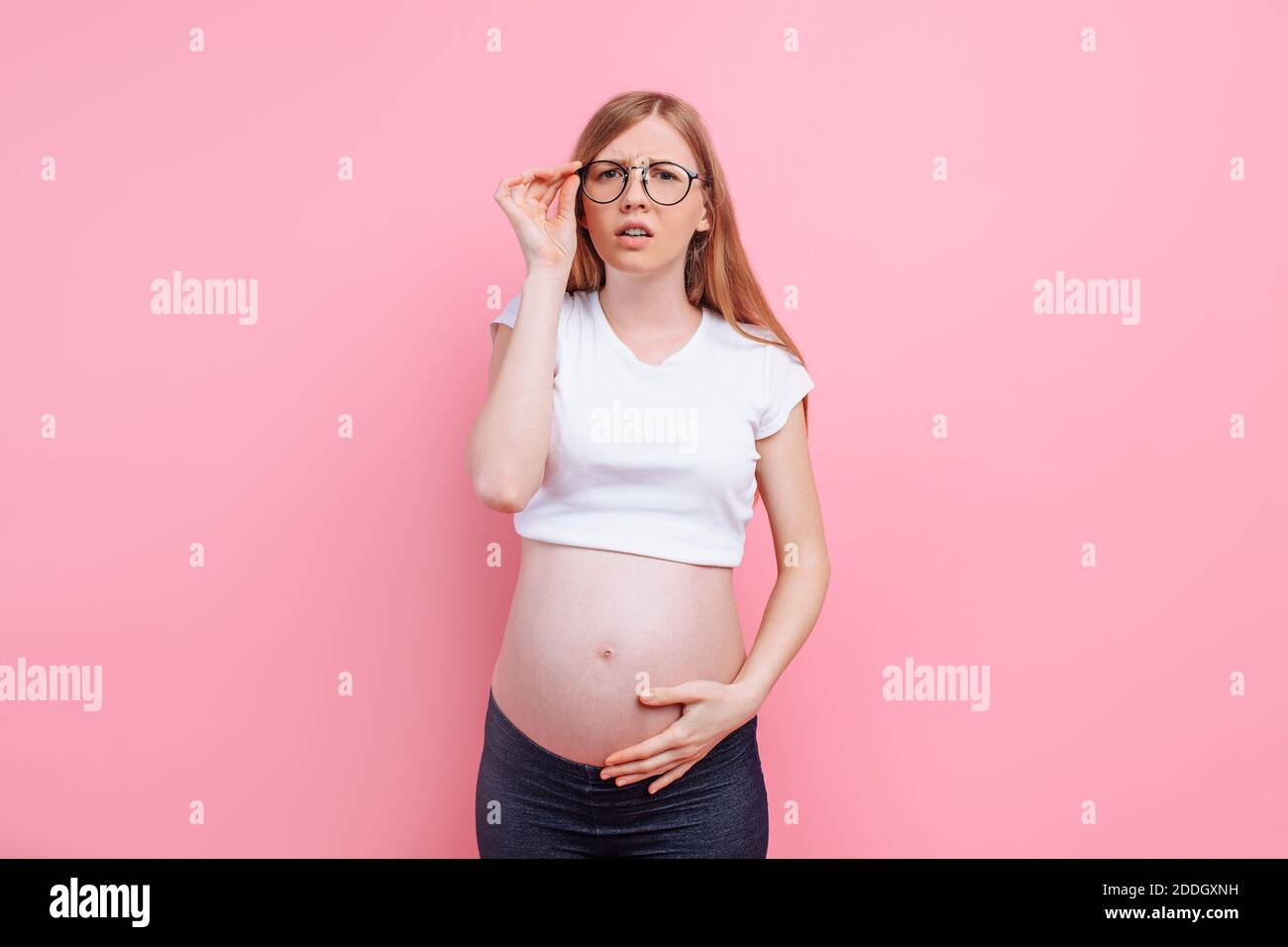 Pregnant girl in a tshirt with glasses for the visually impaired. on pink background, vision