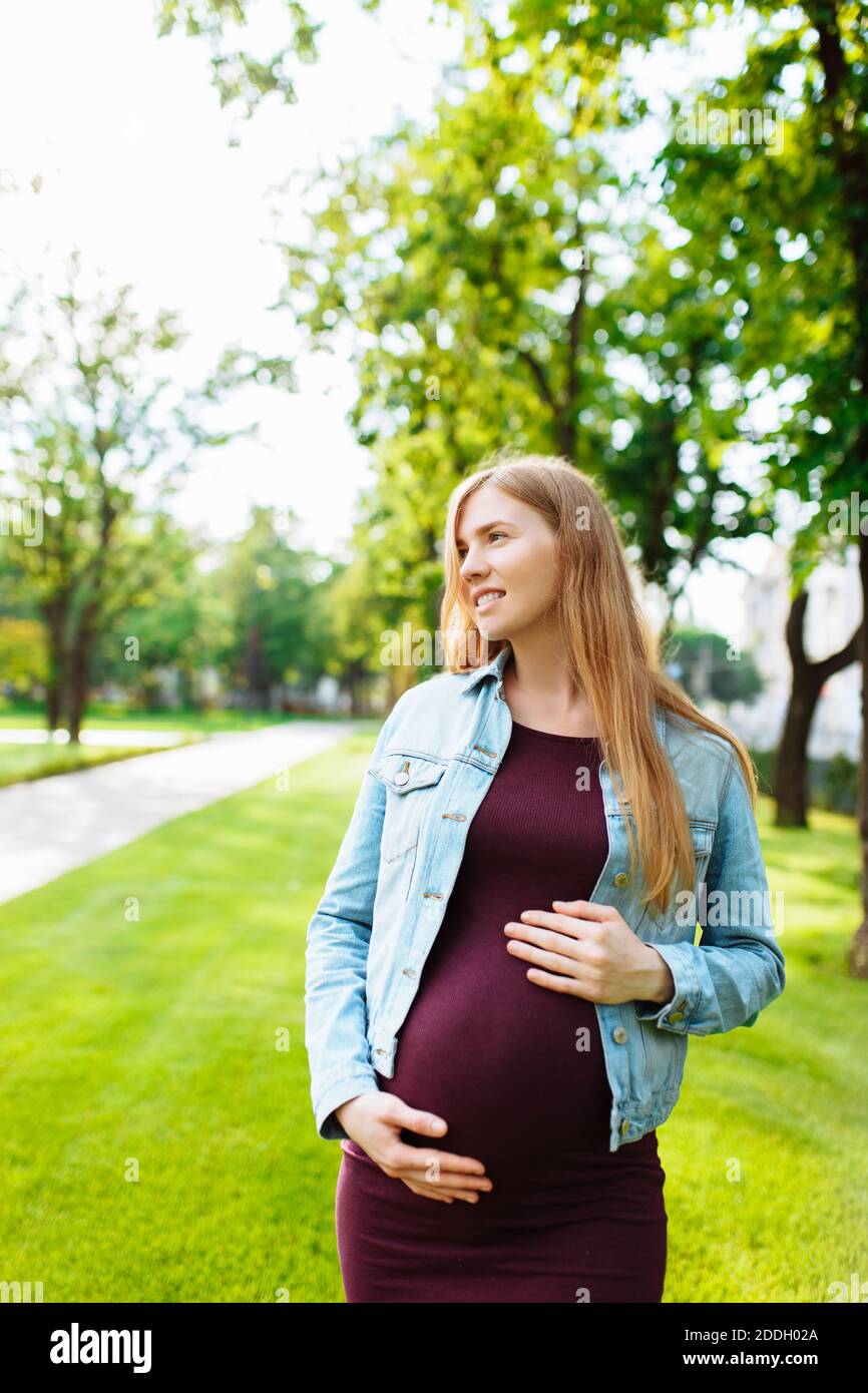 Happy pregnant girl walks in the park, hugging her belly Stock Photo ...