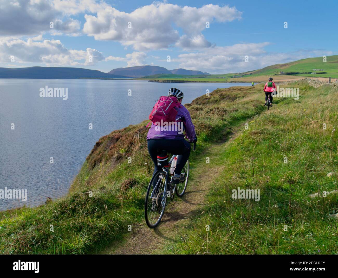 2 females cycling on St Magnus Way coastal trail, Orkney Isles Stock Photo