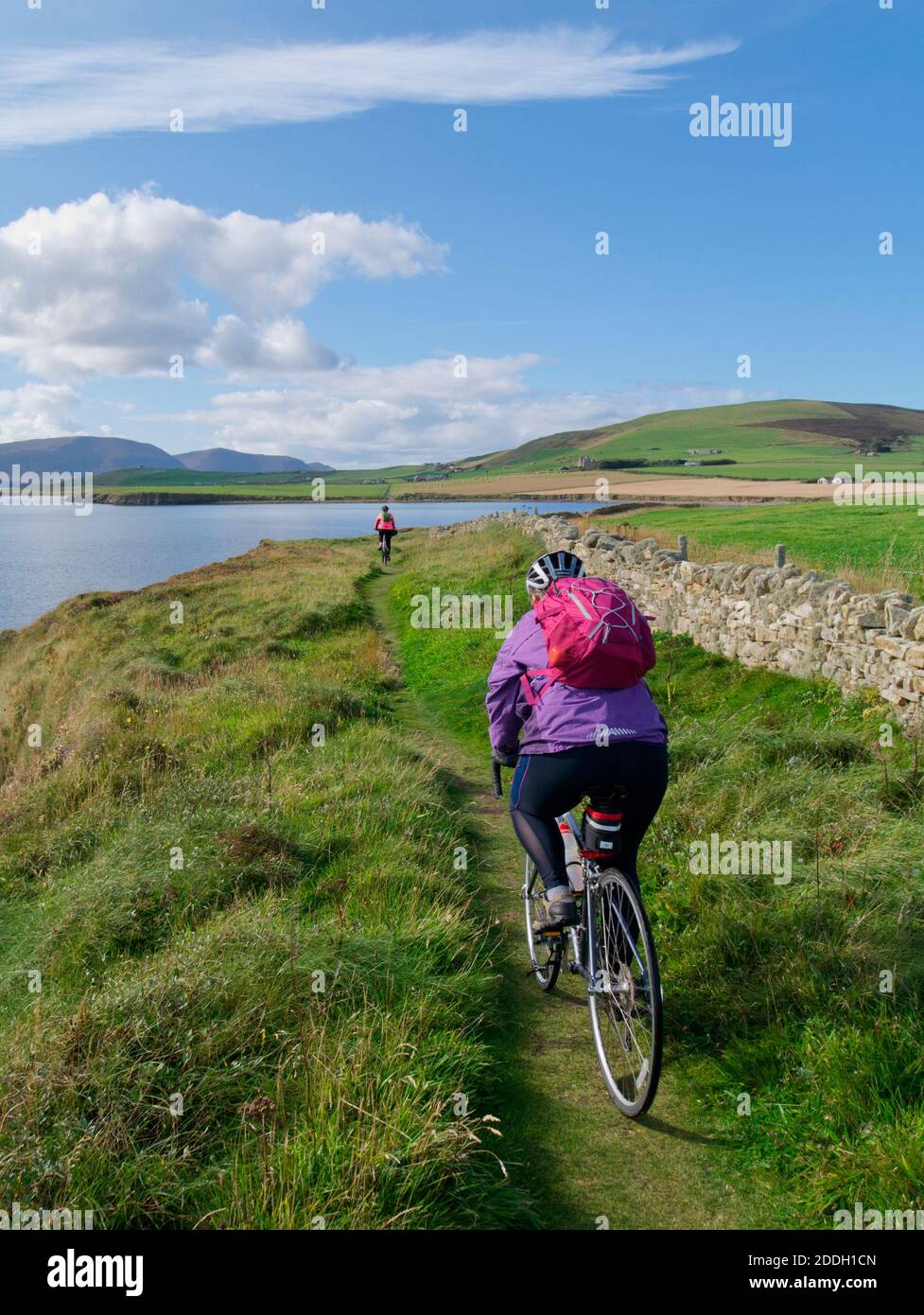 2 females cycling on St magnus Way along Scapa Flow, Orkney Isles Stock Photo
