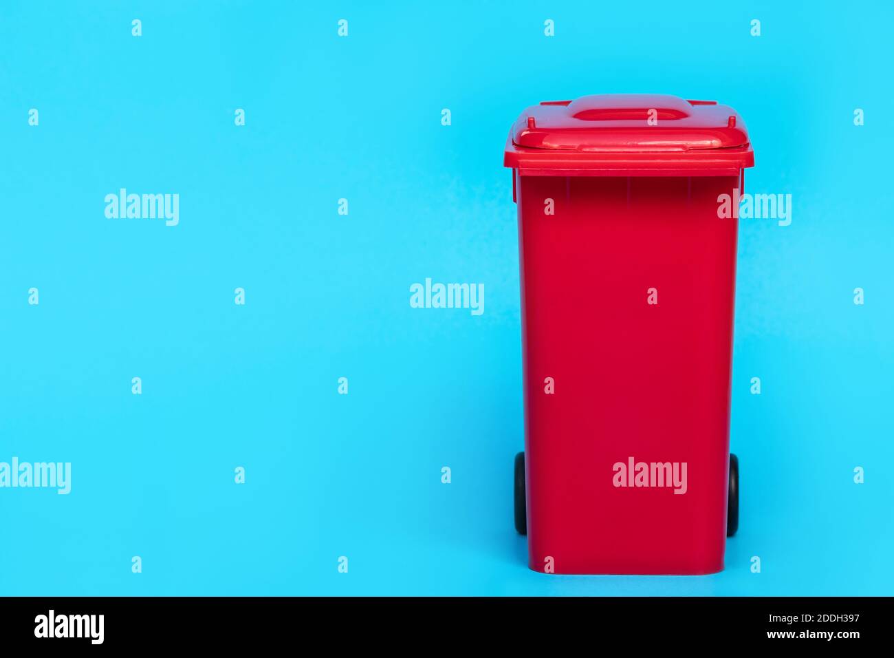 red wheelie waste bin on blue background. Stock Photo
