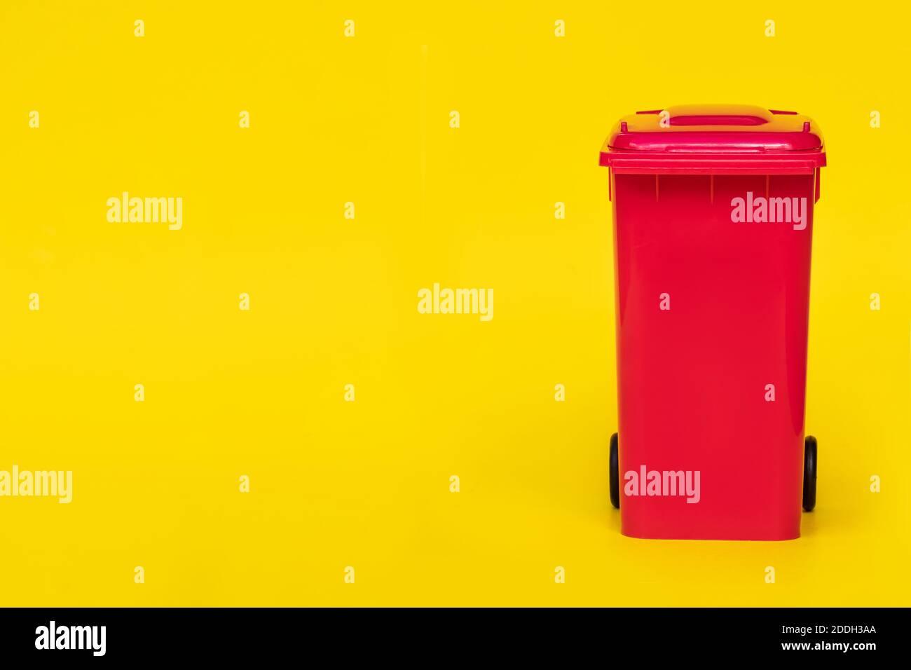 red wheelie waste bin on yellow background. Stock Photo