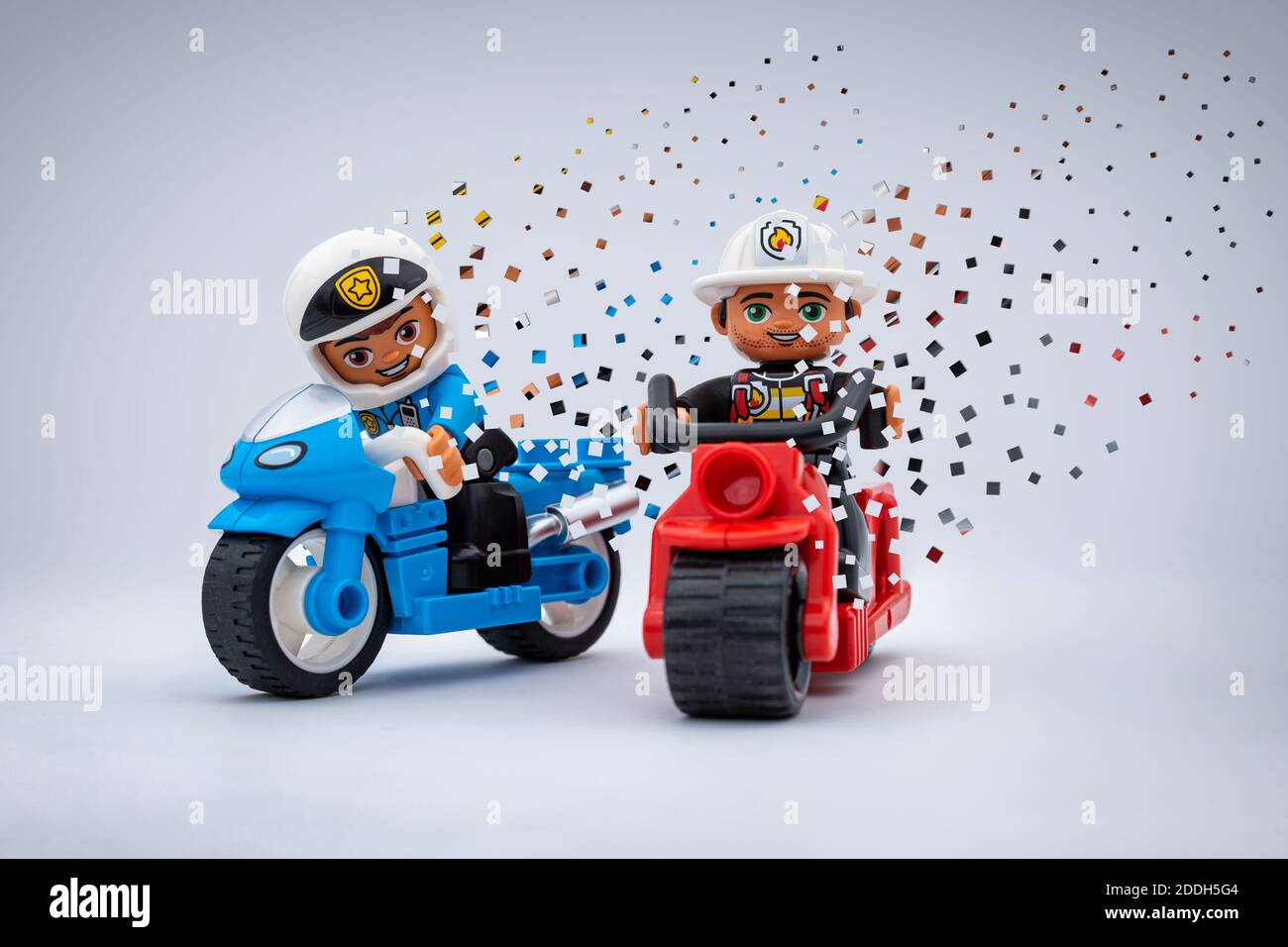 two Lego minifigures motorbikers with a pixelated disintegration effect. A police officer on a blue motorbike and a fireman on a red one. Stock Photo