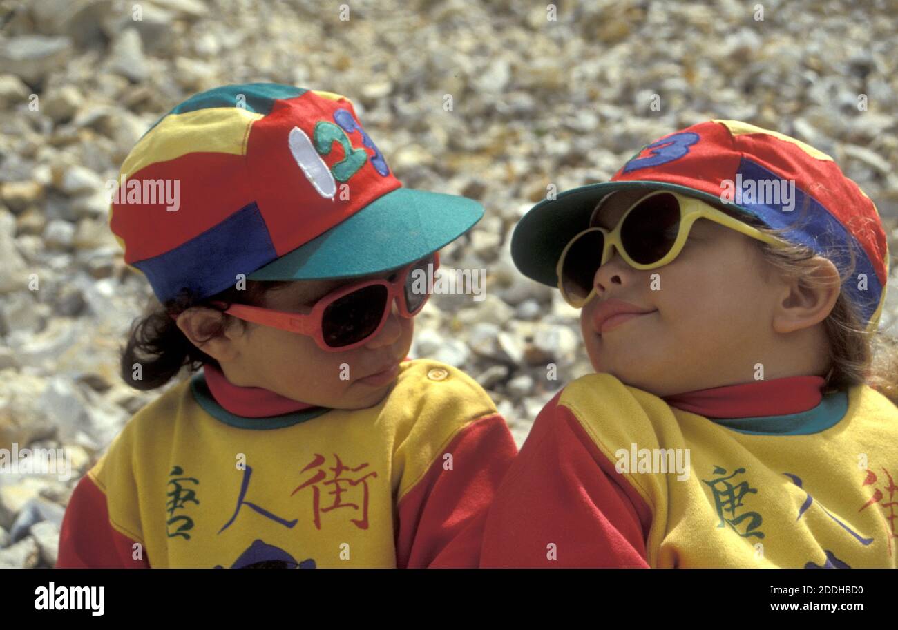 two little sisters in coloured caps and sunglasses looking at each other with attitude Stock Photo