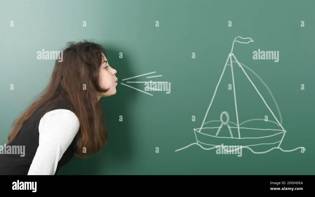 Pre-adolescent girl blowing on painted sailing ship. Portrait photo on school board background. High resolution photo. Full depth of field. Stock Photo