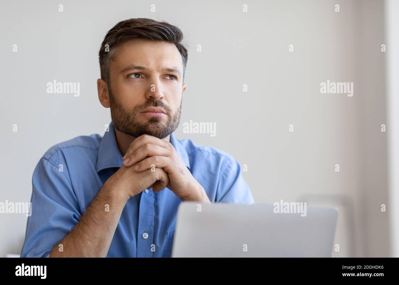 Portrait Of Pensive Businessman Sitting At Workplace With Laptop And Looking Away Stock Photo