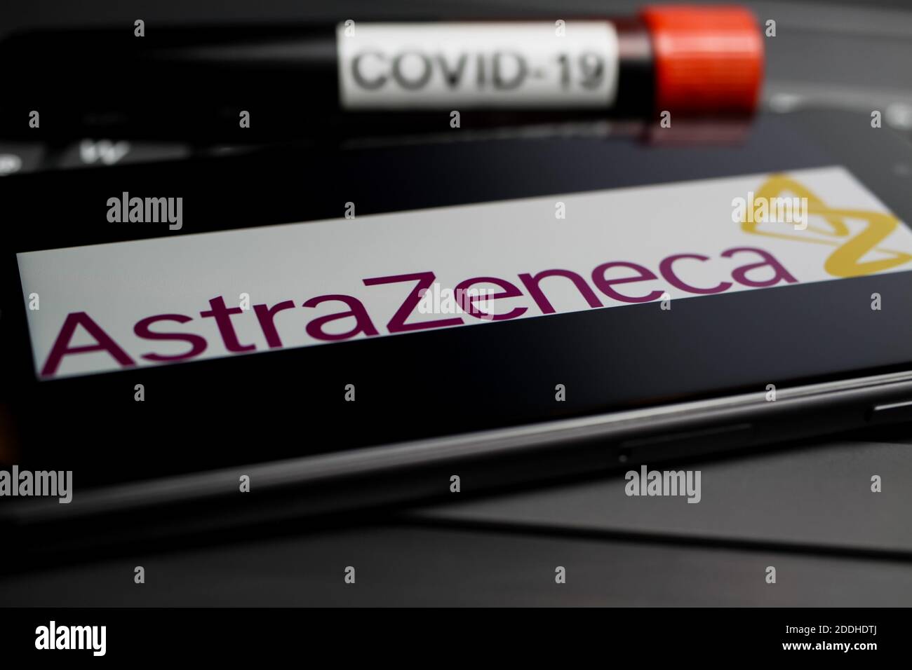 Viersen, Germany - November 9. 2020: Close up of mobile phone screen with logo lettering Astra Zeneca on computer keyboard with covid-19 blood sample Stock Photo