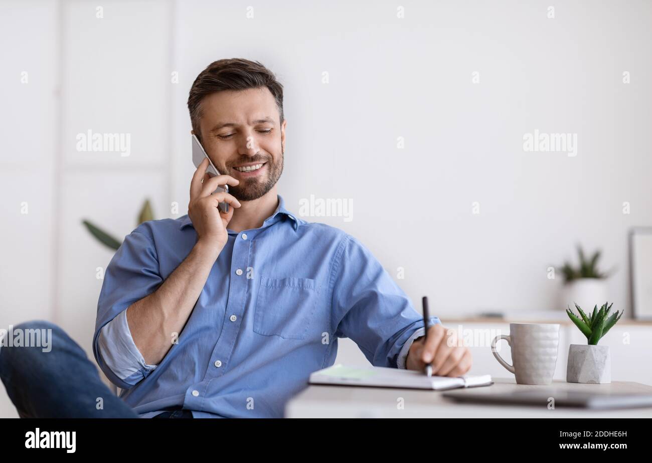 Handsome Businessman Talking On Cellphone And Taking Notes While Working In Office Stock Photo
