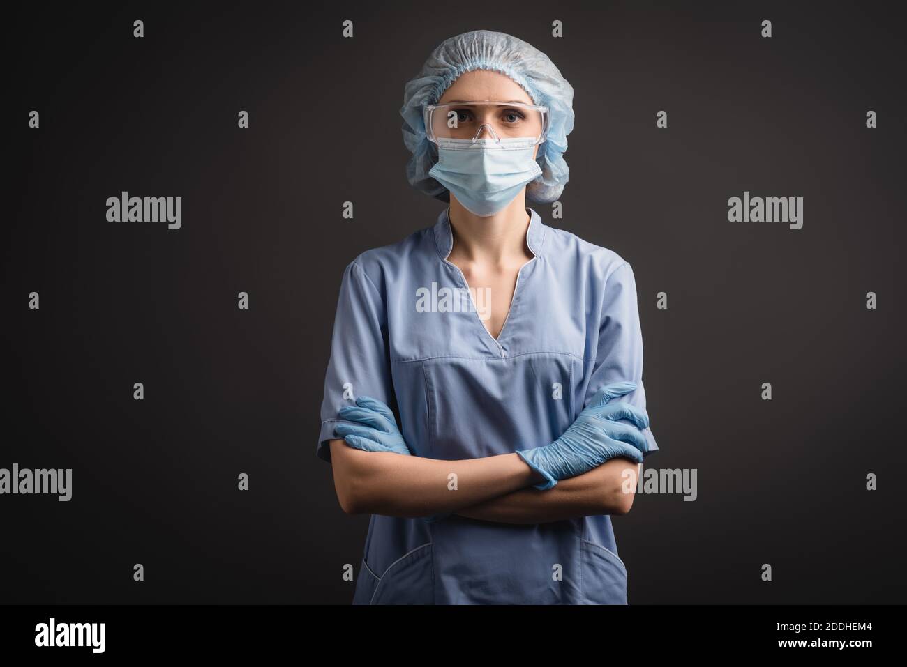 nurse in medical cap, mask and goggles standing with crossed arms and ...