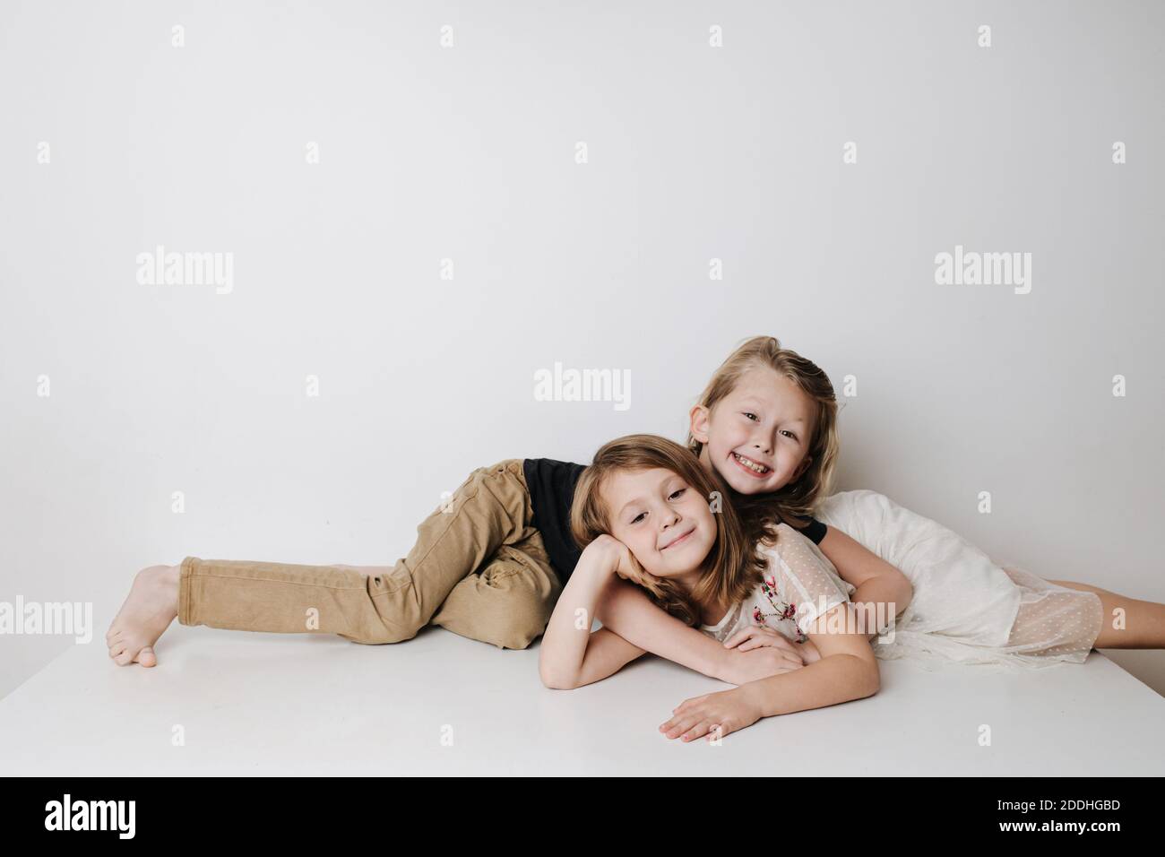 Cheery siblings lie together on a table in opposite directions. Boy hugs girl Stock Photo