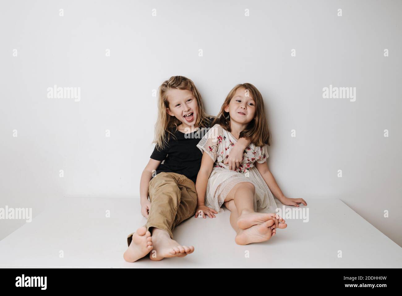 Naughty boy hugs girl, she leans away. Siblings sitting together on a table. Stock Photo