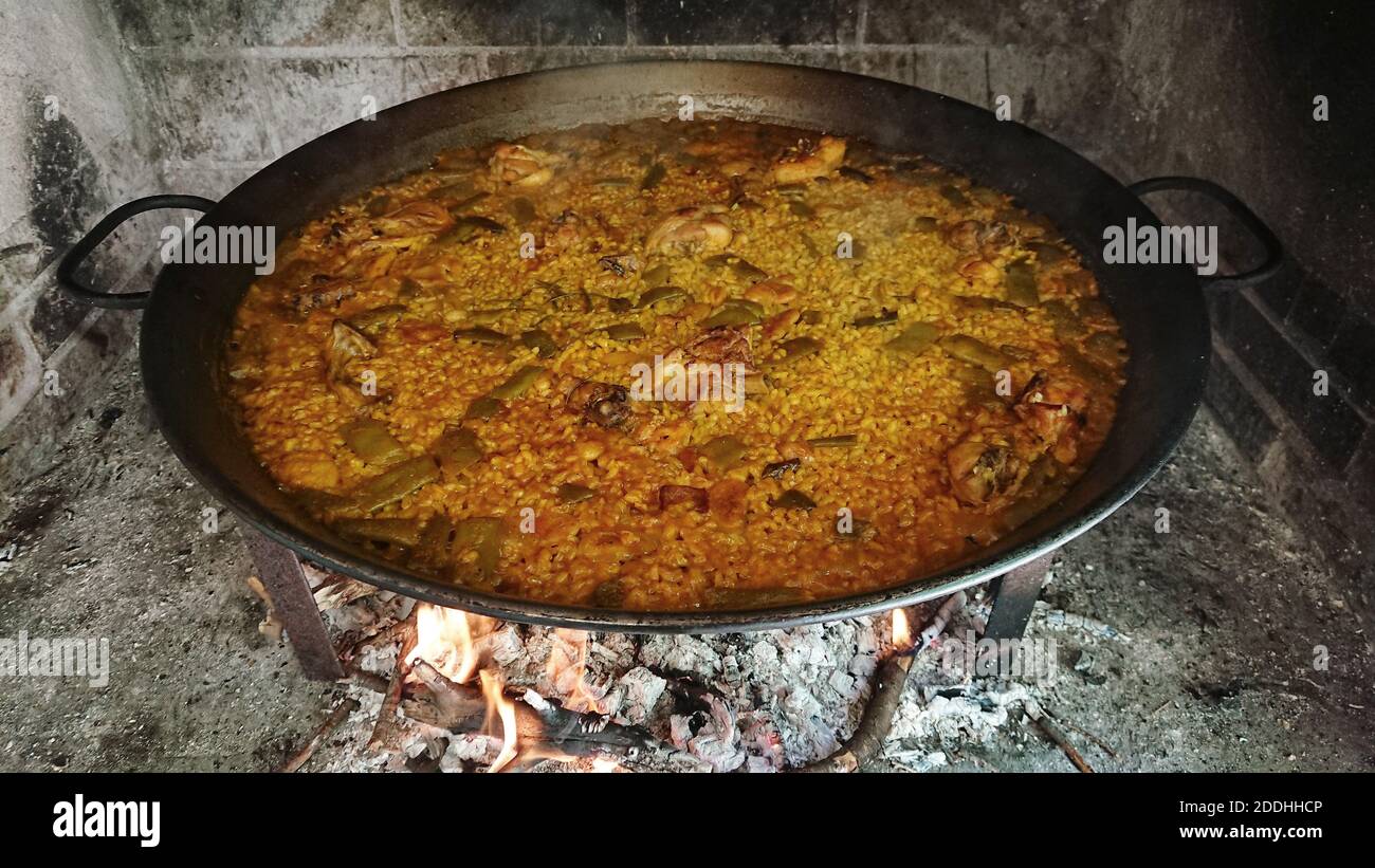 A Closeup of Paella in a big bowl cooking on the fire outdoors Stock Photo