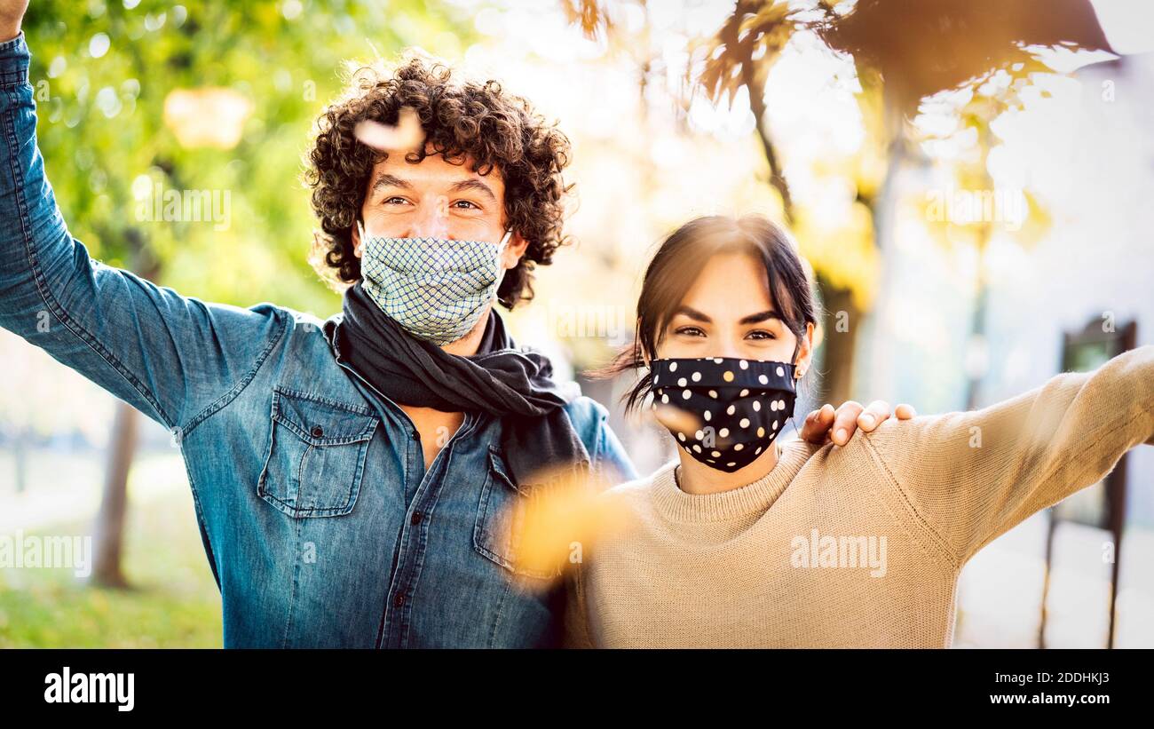 Happy couple of lovers enjoying autumn travel time outdoor wearing protective mask - New normal love concept with boyfriend and girlfriend having fun Stock Photo