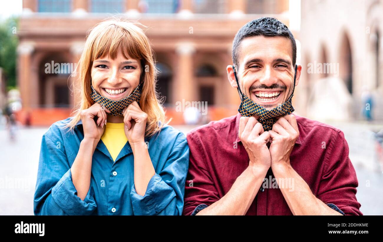 Happy couple smiling with opened face mask after lockdown reopening - New normal relationship concept with guy and girl having fun together Stock Photo