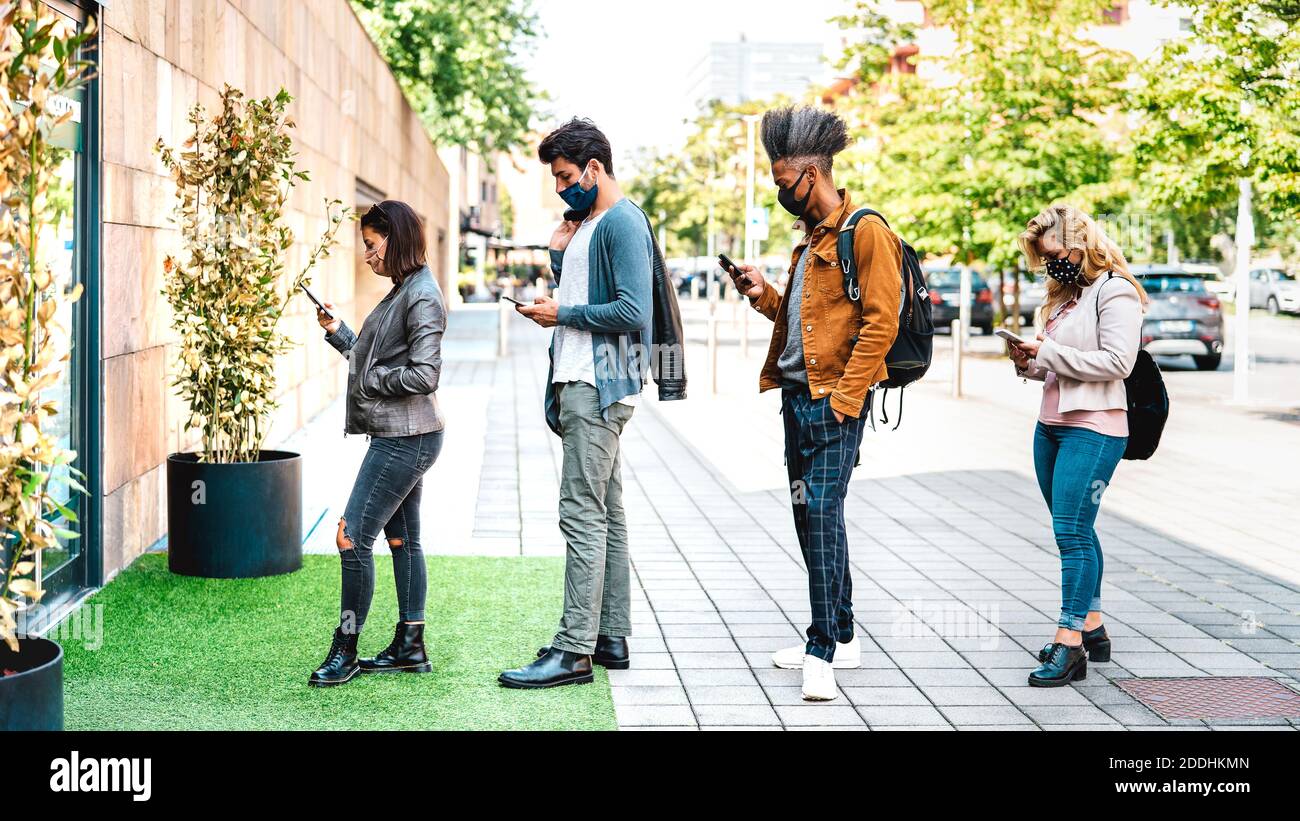 Young people waiting in line practising social distancing at city shop - New normal lifestyle concept with people wearing face mask on urban queue Stock Photo