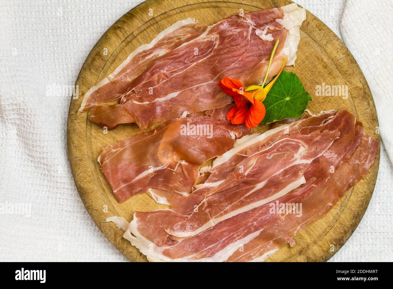 prosciutto slices on rustic wooden board with caper leaf and flower - top view image with copy space Stock Photo