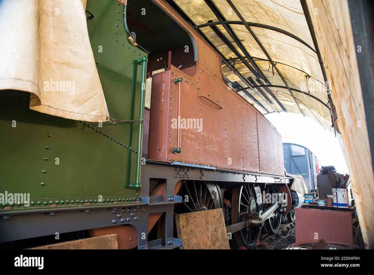 Side close up of vintage UK steam locomotive engine under shelter being renovated. British railways renovation & restoration work. Stock Photo