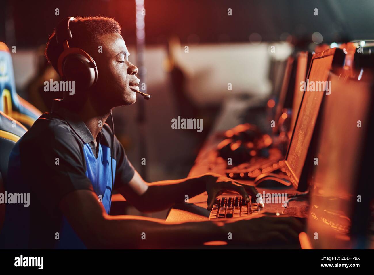Wishing to win. Side view of a young african guy, male professional gamer wearing headphones keeping eyes closed while playing online video game. Participating in eSport tournament Stock Photo