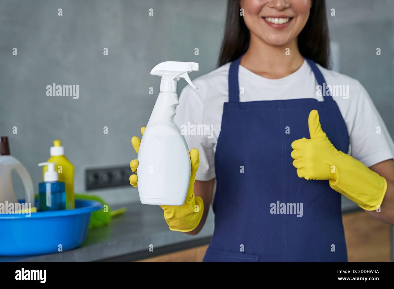 Cropped shot of smiling woman, cleaning lady showing thumbs up while holding household cleaning product, ready for cleaning the house. Housework and housekeeping, cleaning service concept Stock Photo