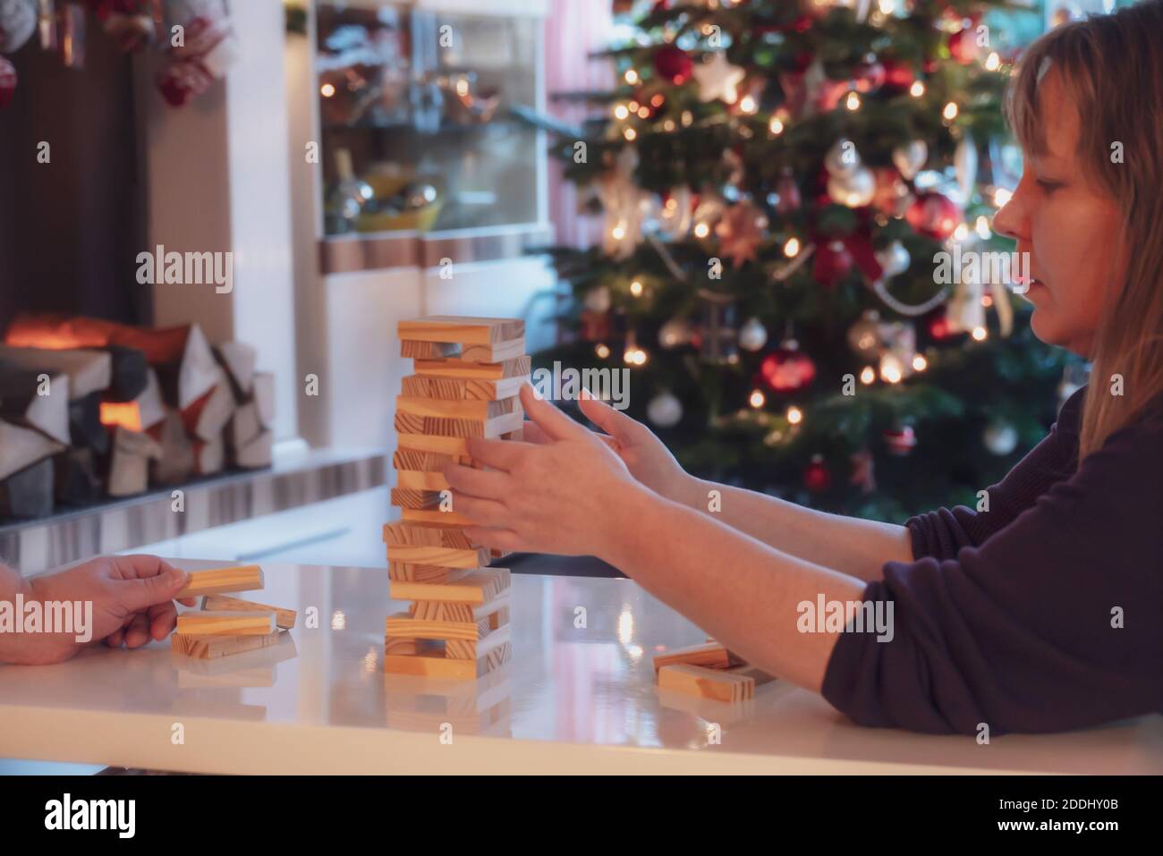 During the Christmas season, the family plays board games together. Woman and man build a wobbly tower from wooden blocks. In the background is the Ch Stock Photo