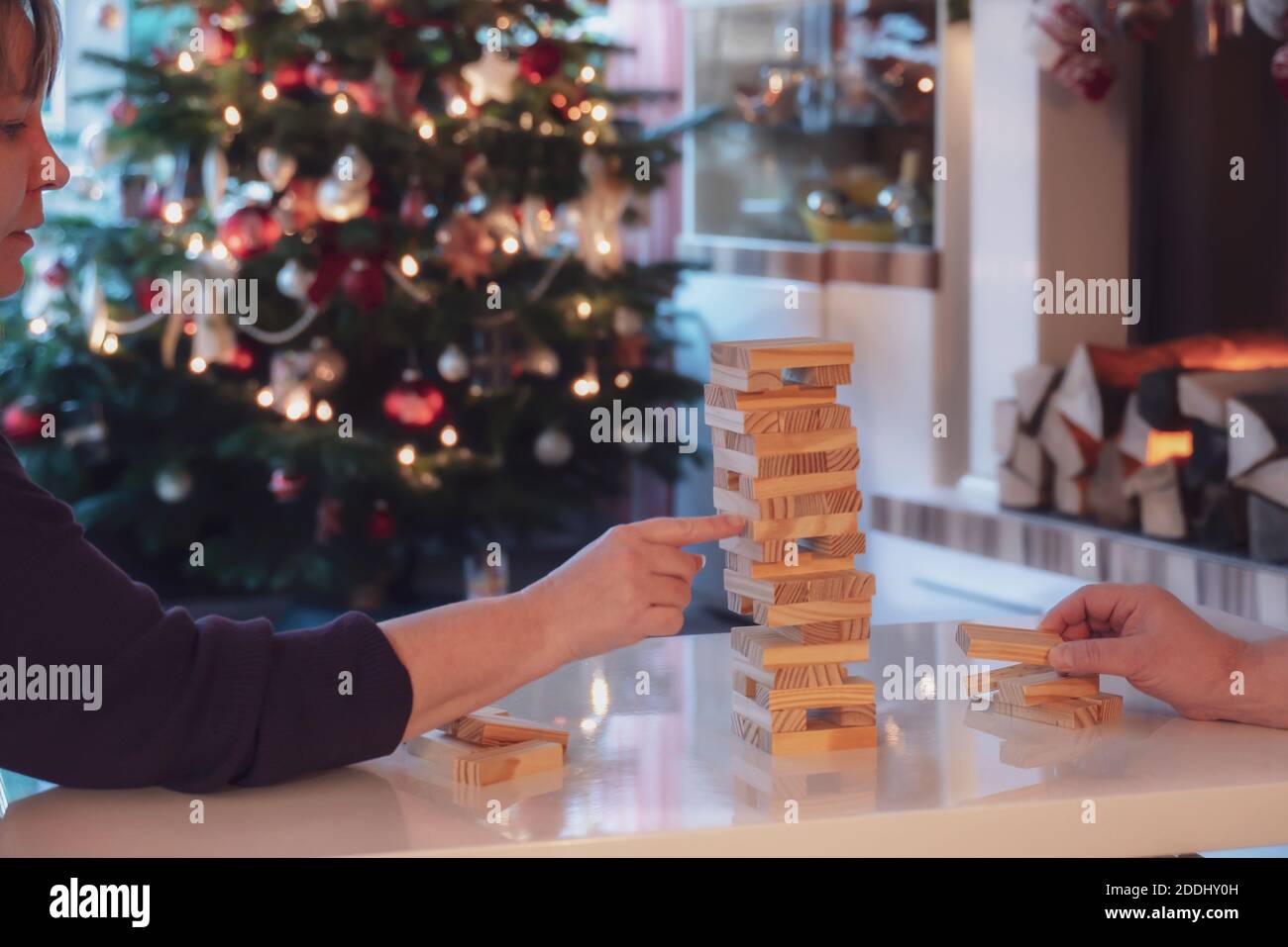 During the Christmas season, the family plays board games together. Woman and man build a wobbly tower from wooden blocks. In the background is the Ch Stock Photo