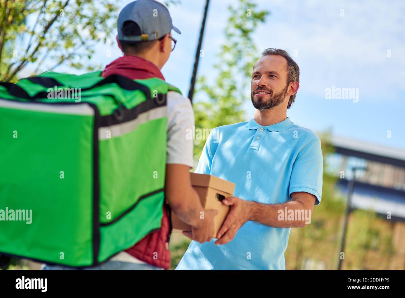 Male courier with thermo bag delivering parcel to customer while