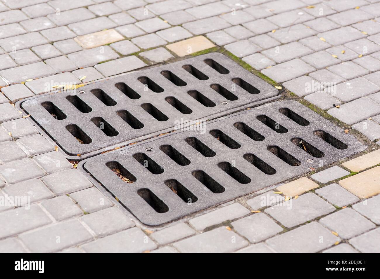 the square iron grating of the rainwater hatch cover on the stone tile pedestrian sidewalk, closeup side view of the drainage system. Stock Photo