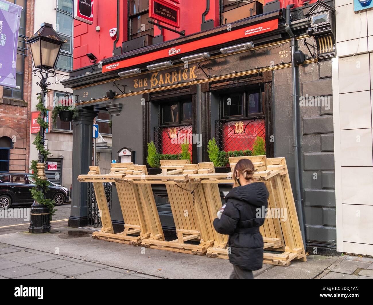 Belfast, Northern Ireland, UK, 25 November 2020: A girl walks past tables stacked outside the Garrick Bar, Chichester Street as lock down looms Stock Photo