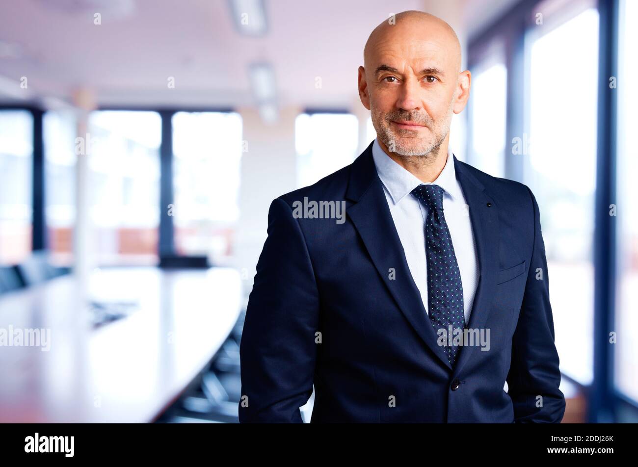 Portrait shot of smiling businessman wearing suit and tie while standing in the conference room. Stock Photo