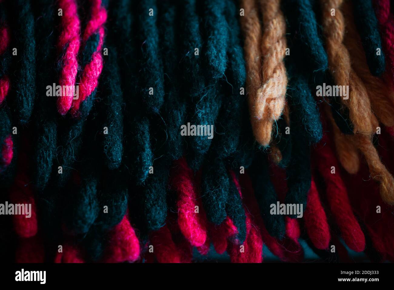 Cold season home warmth and cosiness. Woolen braided thick threads tassels of a warm traditional plaid, group of many hanging knitted red, yellow and Stock Photo