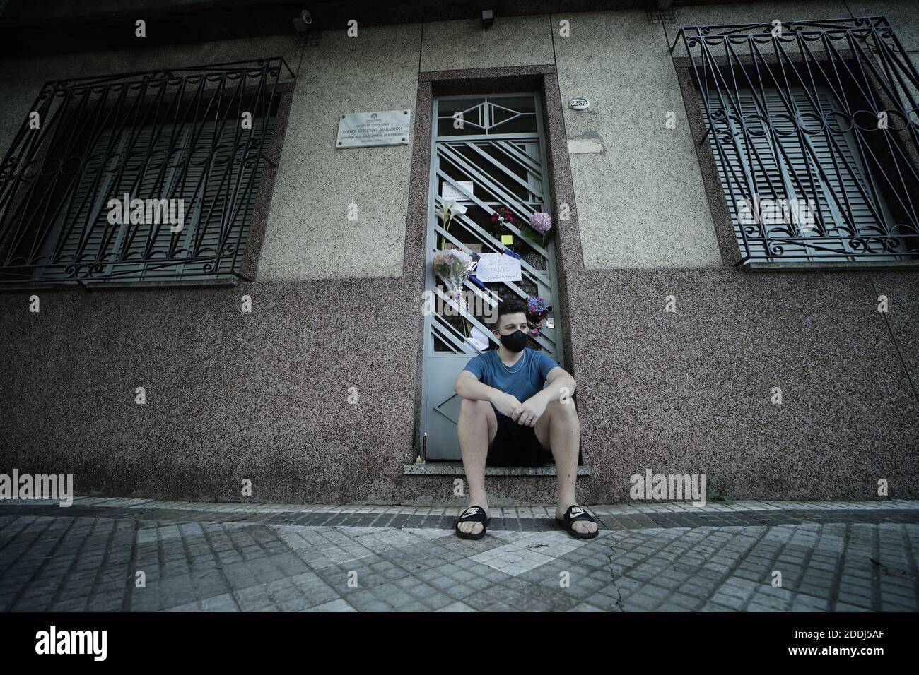 Buenos Aires, Argentina. 25th Nov, 2020. A young man sits at the door of Maradona's former residence in the La Paternal district after it became known that the football legend had died. Maradona lived in this house in the late 1970s when he played for the Argentinos Juniors football club. Credit: Gustavo Ortiz/dpa/Alamy Live News Stock Photo