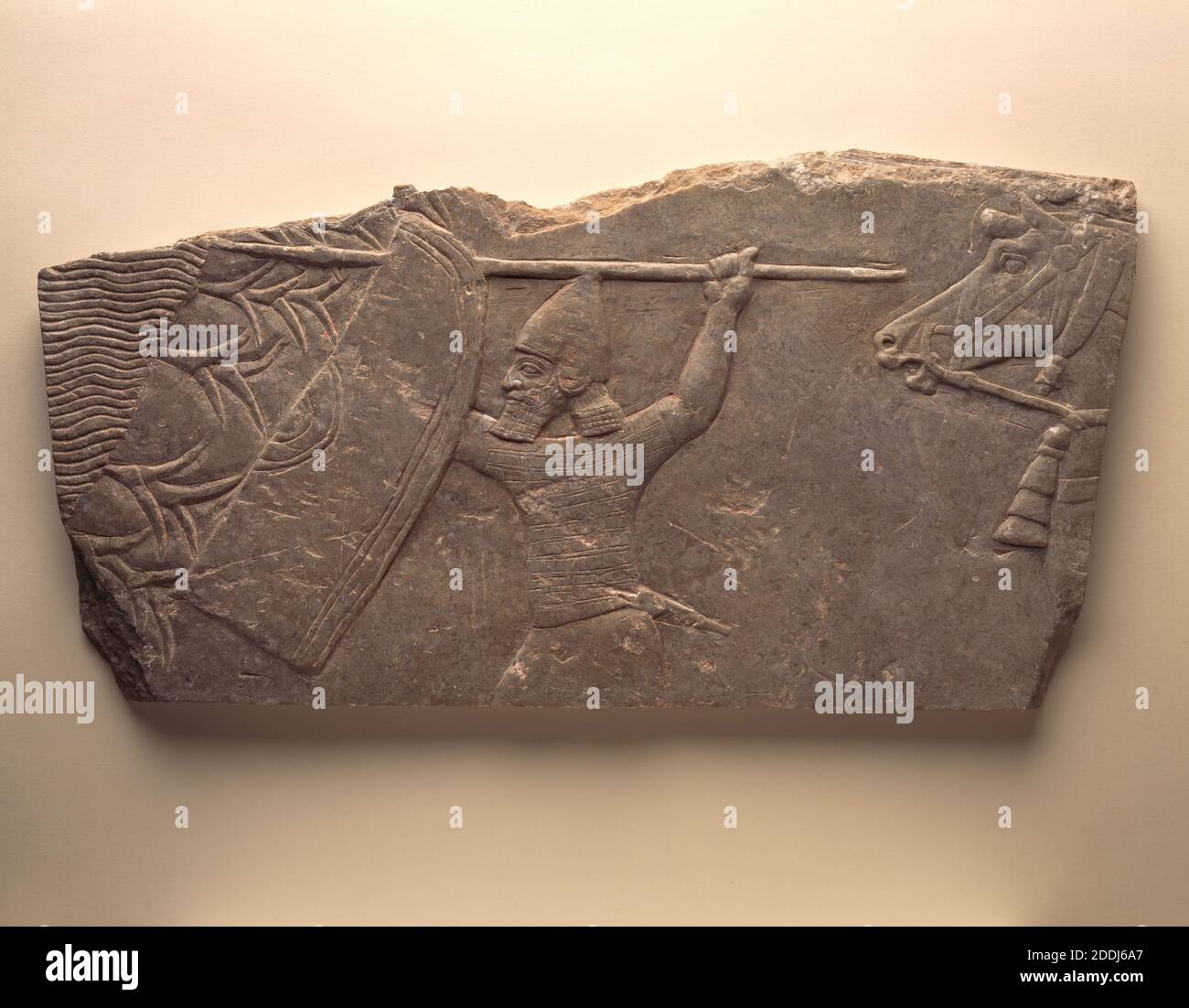 Fragment of a Carved Relief from a Palace Wall, 668 BC-627 BC Iraq, Nineveh h522 x w285 x d26 mm, Flat limestone slab showing Assyrian lancer advancing left into reeds by the side of a marsh of pool., Asia, Western Asiatic, Armour, Middle East, Architecture, Animal, Horse, Relief, Antiquities, Ancient Civilisations, Soldier, Stone Carving, Stone, Limestone Stock Photo